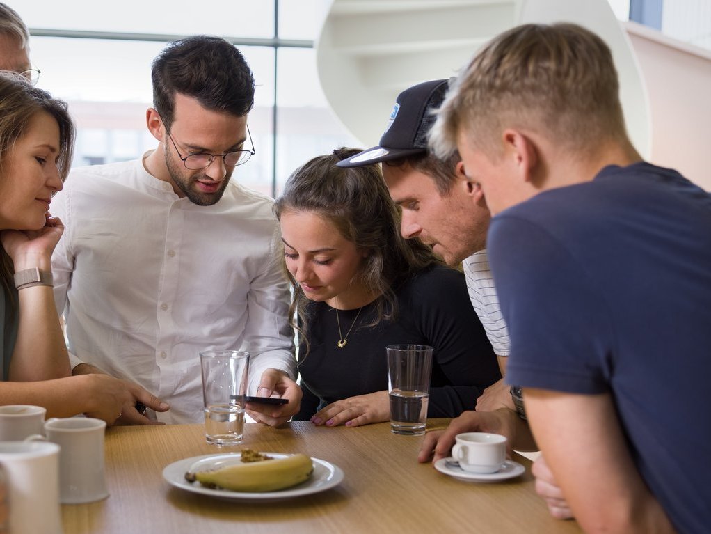 Colleagues are standing at a nice table in the coffee kitchen, looking at a smartphone with interest.