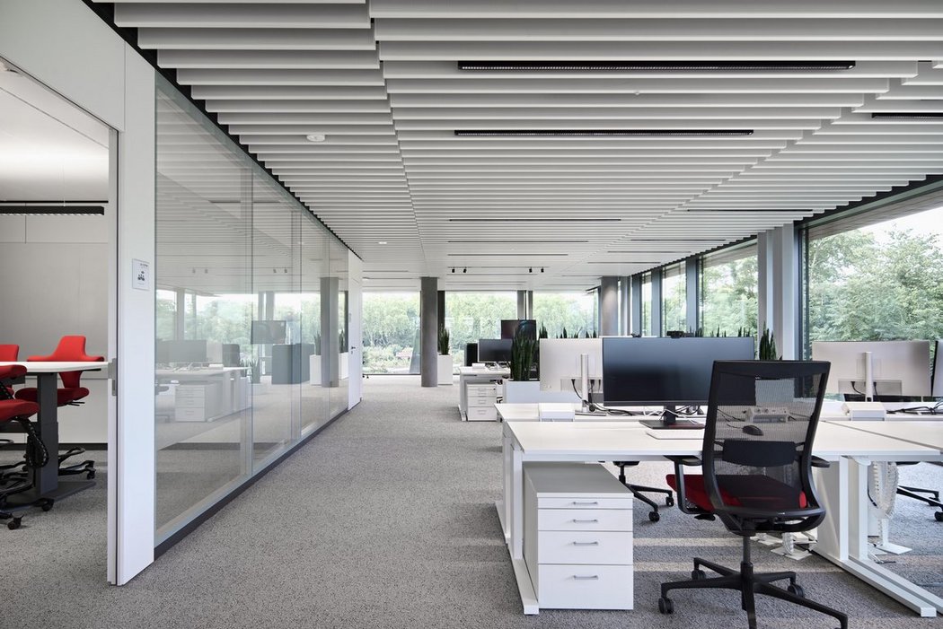 Lichtdurchflutetes Büro mit höhenverstellbaren Schreibtischen und großen Curved-Monitoren. Im Hintergrund ist eine grüne Landschaft.