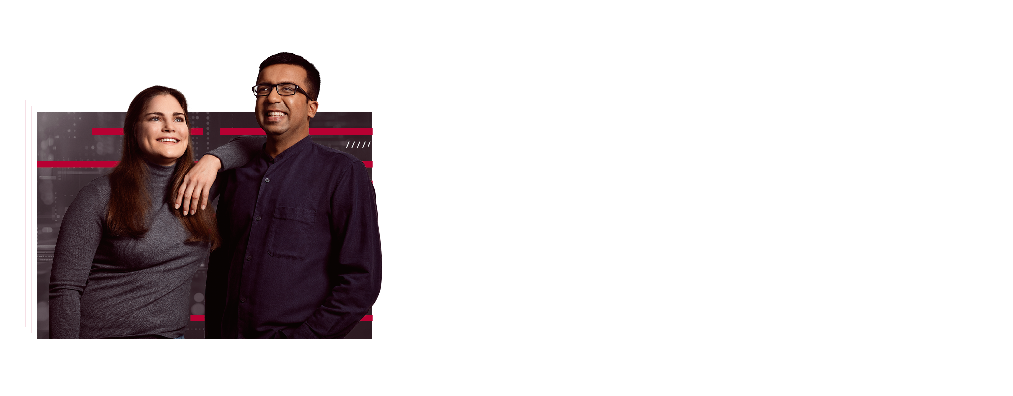 Two employees are standing next to each other. She has one arm on her colleague's shoulder. Both are smiling and appear content.