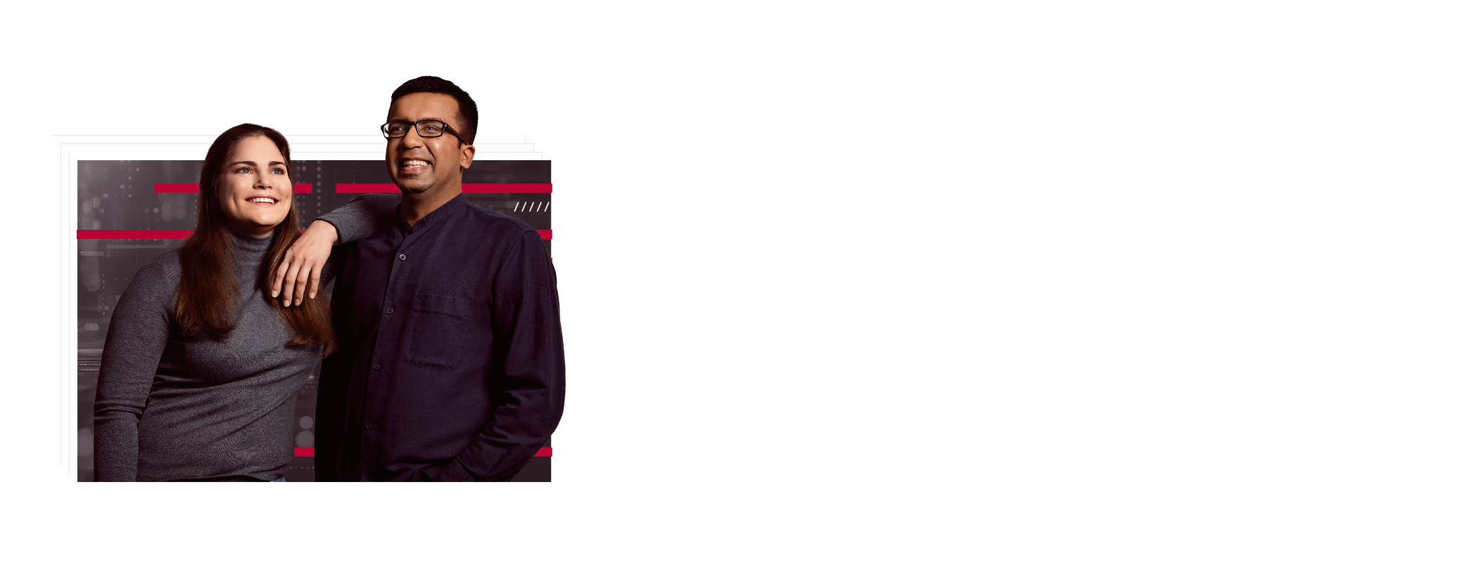 Two employees are standing next to each other. She has one arm on her colleague's shoulder. Both are smiling and appear content.