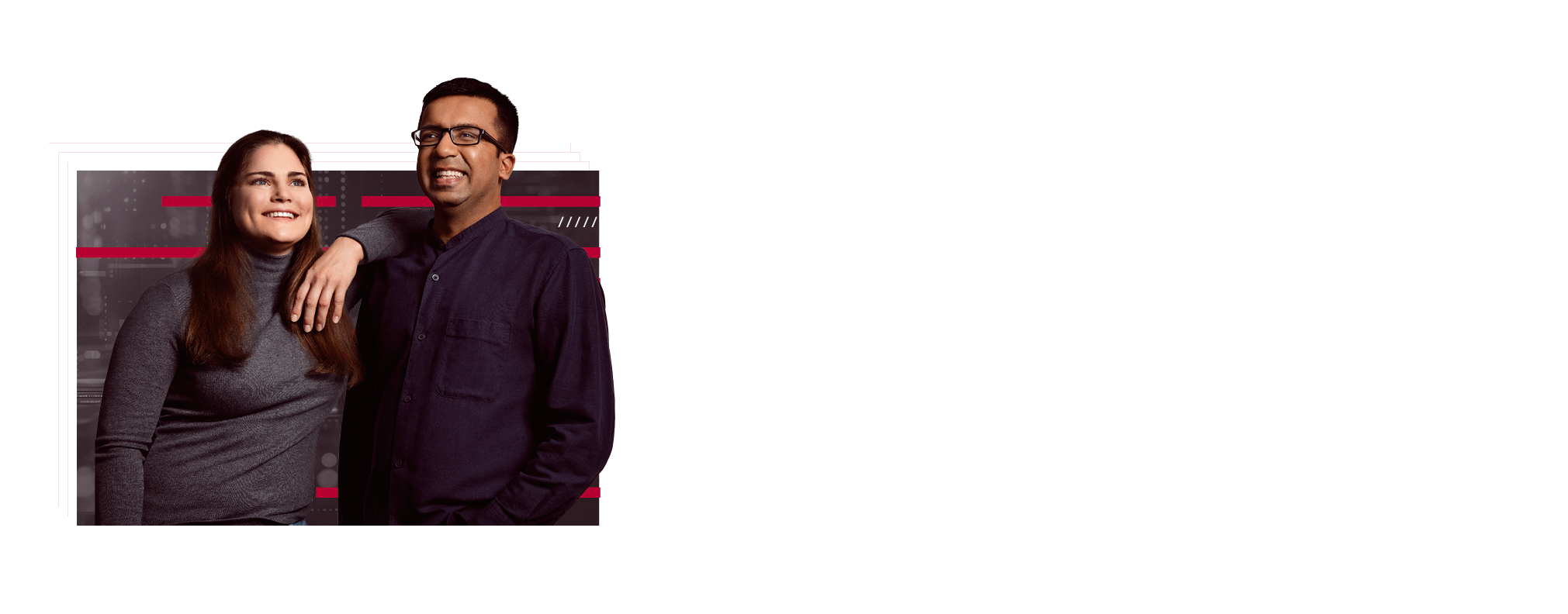 Two employees are standing next to each other. She has one arm on her colleague's shoulder. Both are smiling and appear content.