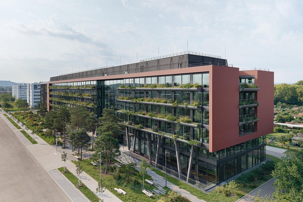 Neues Bürogebäude mit begrünter Fassade Glasfassade und Balkonen, umgeben von grüner Vegetation bei Sonnenuntergang.