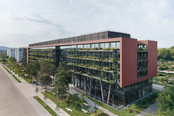 Neues Bürogebäude mit begrünter Fassade Glasfassade und Balkonen, umgeben von grüner Vegetation bei Sonnenuntergang.
