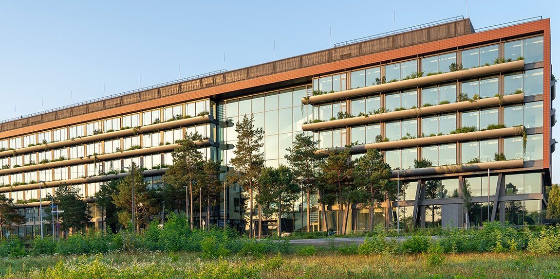 New office building with green facade Glass facade and balconies, surrounded by green vegetation at sunset.
