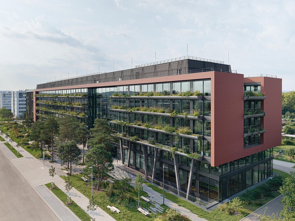Neues Bürogebäude mit begrünter Fassade Glasfassade und Balkonen, umgeben von grüner Vegetation bei Sonnenuntergang.