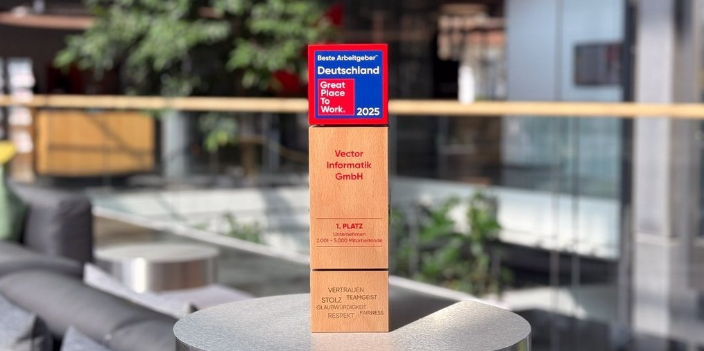 Moderne Büro-Umgebung mit gemütlichen Sitzgelegenheiten und einer grünen Pflanze im Hintergrund. Im Vordergrund steht eine Auszeichnung aus Holz mit Titel "Beste Arbeitgeber Deutschland – Great Place to Work 2025“.