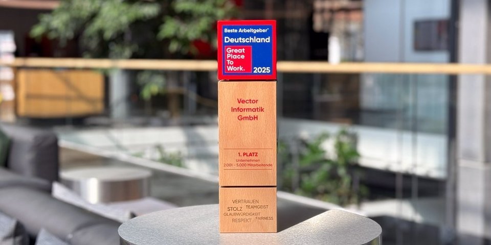 aModerne Büro-Umgebung mit gemütlichen Sitzgelegenheiten und einer grünen Pflanze im Hintergrund. Im Vordergrund steht eine Auszeichnung aus Holz mit Titel "Beste Arbeitgeber Deutschland – Great Place to Work 2025“.