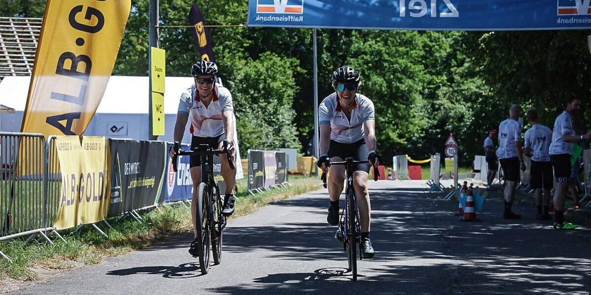 Two employees cross the finish line of the Alb-Extrem cycling event wearing Vector jerseys, smiling in the bright sunshine.