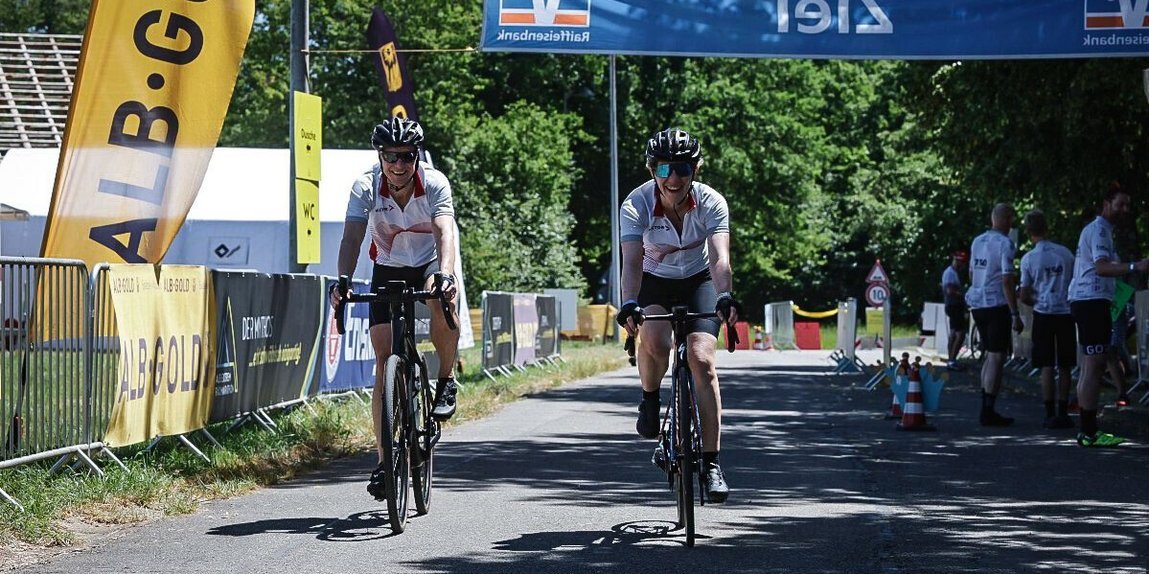 Zwei Mitarbeitende überqueren bei strahlendem Sonnenschein lächelnd die Ziellinie des Rad-Events Alb-Extrem mit Vector-Trikot.
