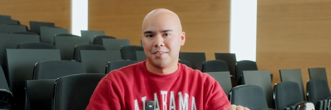 A Vector employee wearing a red sweatshirt is sitting in a modern auditorium. An American football is lying in front of him.