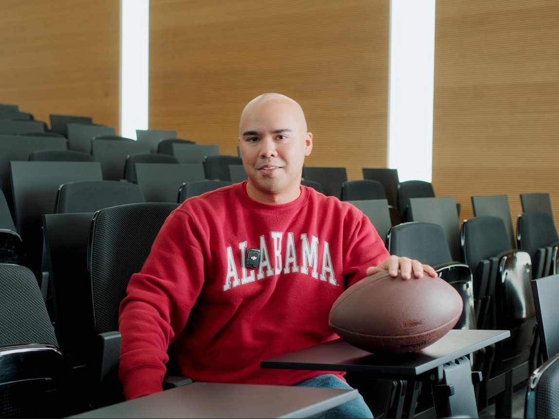 Ein Vector-Mitarbeiter in einem roten Sweatshirt sitzt in einem modernen Auditorium. Vor ihm liegt ein American Football.
