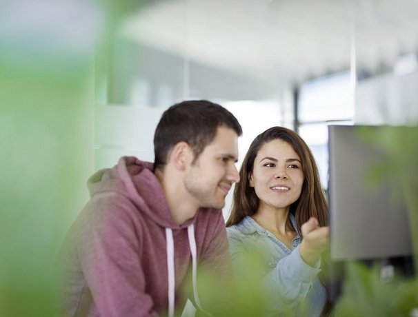 Zwei Vector Mitarbeitenden die vor einem PC Bildschirm sitzen und sich freundlich unterhalten  