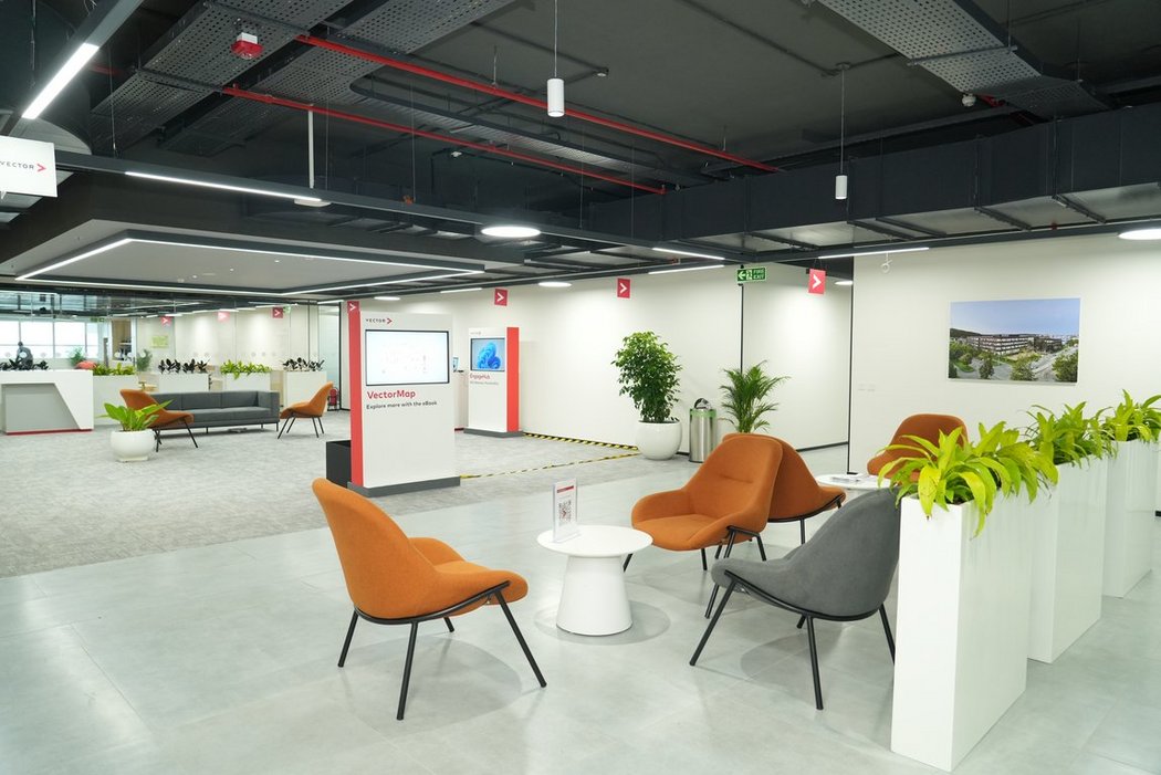 Large, open lounge area with designer armchairs, plants, and digital information kiosks. The generous glass front and subtle lighting emphasize the modern, inviting atmosphere.