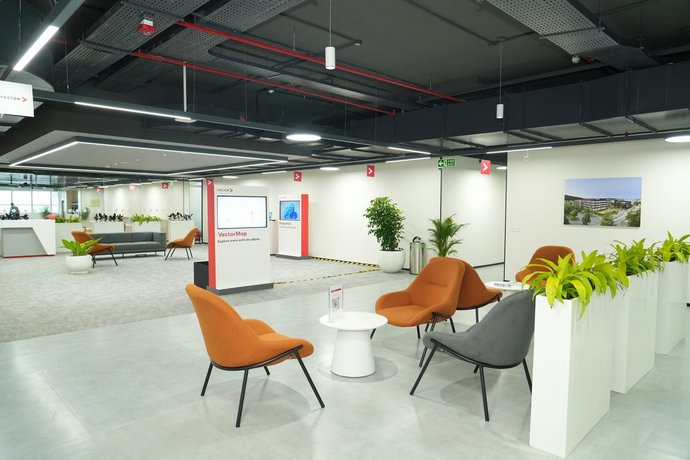Large, open lounge area with designer armchairs, plants, and digital information kiosks. The generous glass front and subtle lighting emphasize the modern, inviting atmosphere.