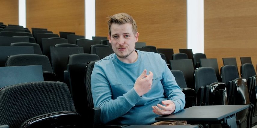 A Vector employee sits in an auditorium and gestures, wearing a blue sweater.