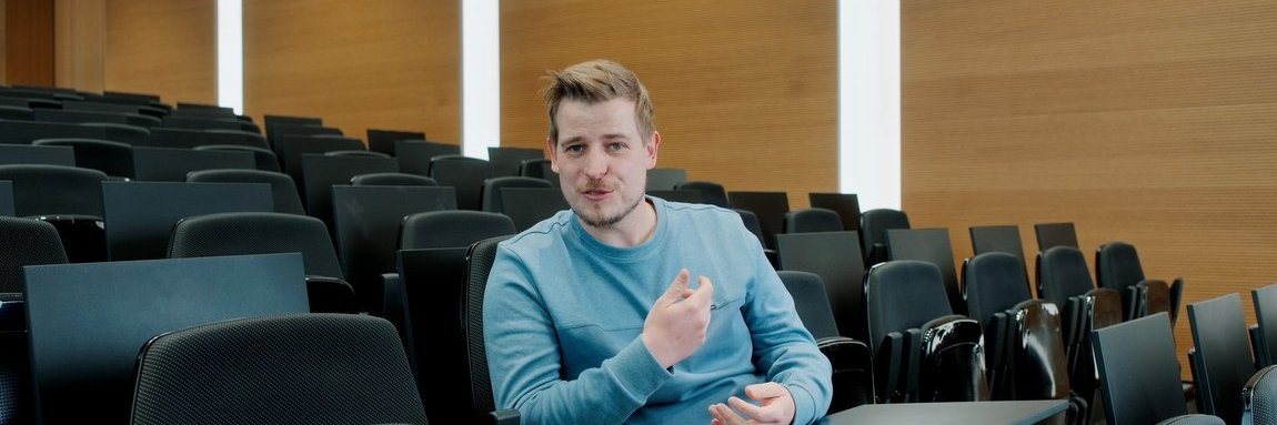 A Vector employee sits in an auditorium and gestures, wearing a blue sweater.