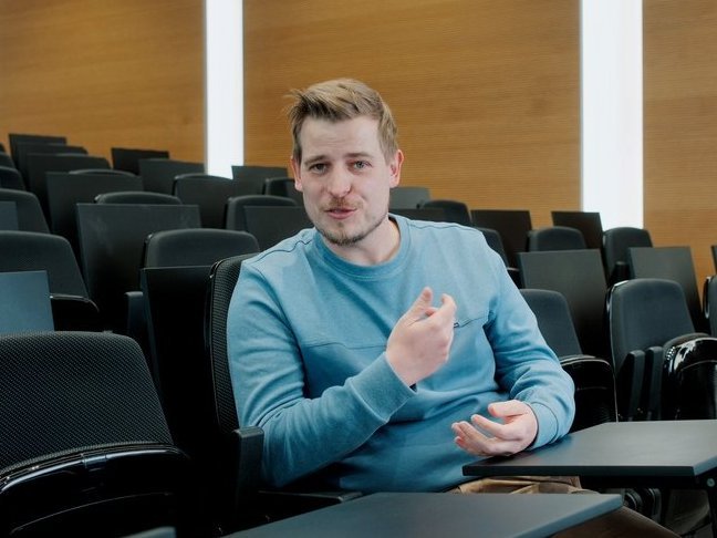 A Vector employee sits in an auditorium and gestures, wearing a blue sweater.