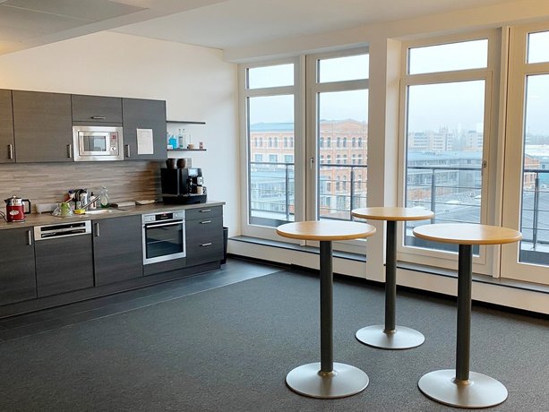 Küche Büroküche mit grauen Schränken, Mikrowelle, Kaffeemaschine und Stadtblick durch große Fenster – drei runde Stehtische im Vordergrund