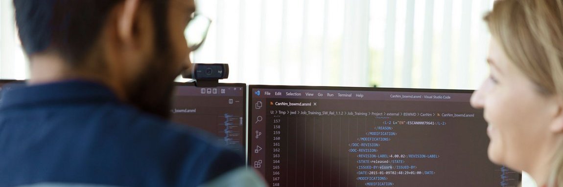 Kollegin und Kollege beim Code-Review vor zwei Monitoren
