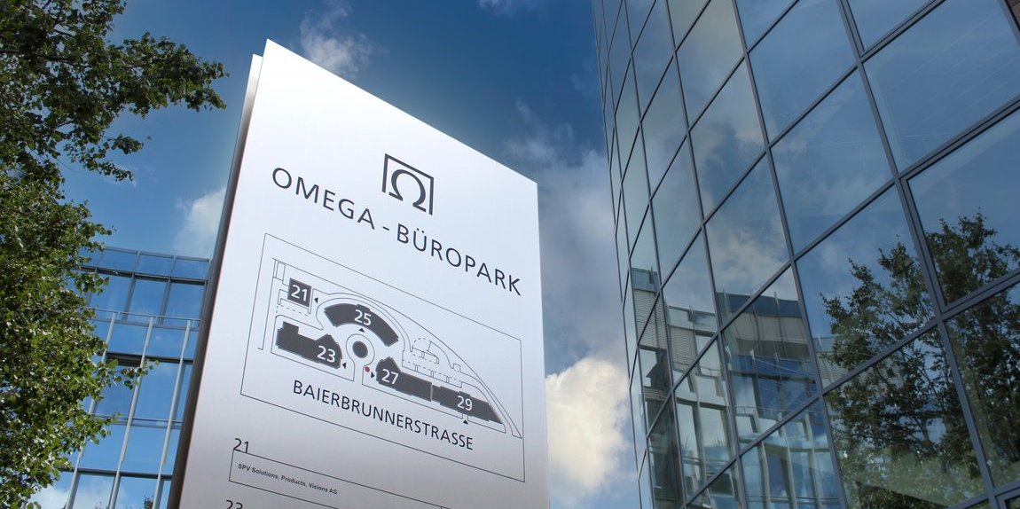 Omega Büropark Schild mit Lageplan und Firmenübersicht an der Baierbrunnerstraße, umgeben von modernen Glasbauten und blauem Himmel