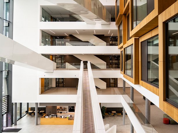 Neues Bürogebäude mit mehreren Etagen, offenen Arbeitsbereichen, großen Fenstern und einer freitragenden Rollrutschen. Innenarchitektur mit Holzverkleidung und minimalistischen Design.