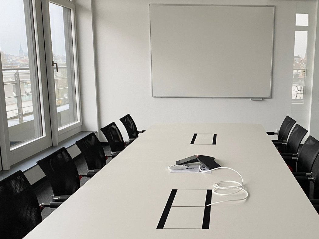 Besprechungsraum Konferenzzimmer mit großem Tisch, schwarzen Stühlen, Konferenztelefon und Whiteboard – helle Fensterfront mit Stadtblick