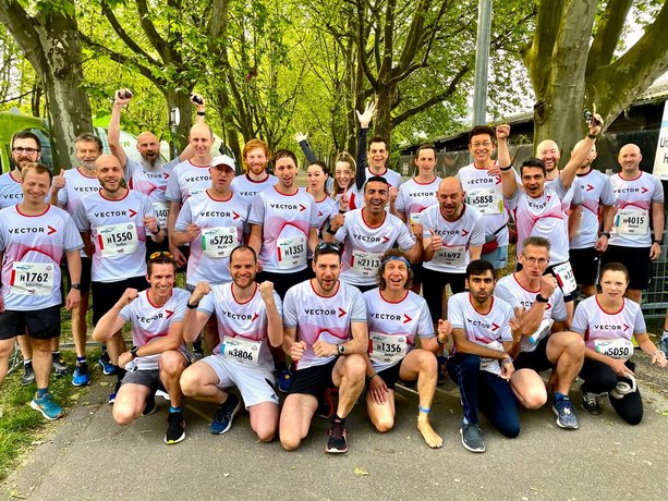 Große Gruppe von Vector-Mitarbeitenden mit schickem Laufshirt freudig lachend vor dem Start.