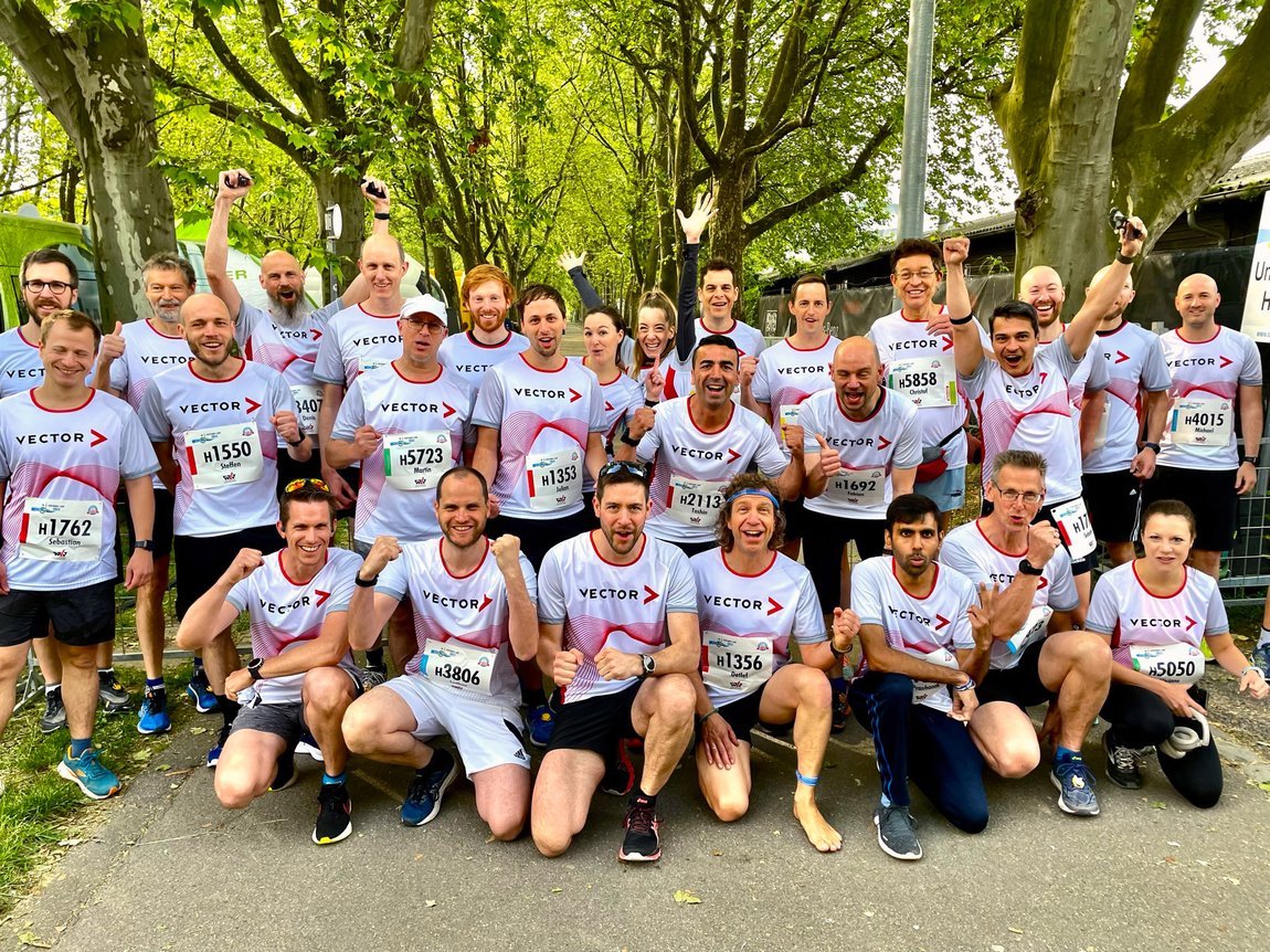 Große Gruppe von Vector-Mitarbeitenden mit schickem Laufshirt freudig lachend vor dem Start.