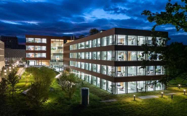 Bürogebäude bei Nacht mit beleuchteten Fenstern, Glasfassade, zeitgemäßem Design und grüner Umgebung