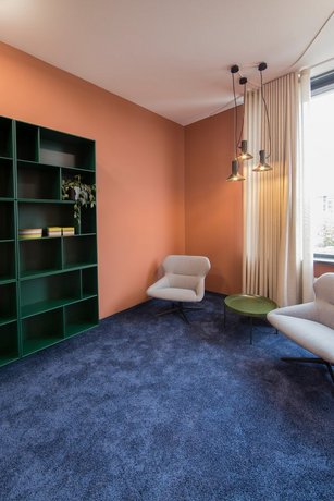 A room with a blue carpet, an orange wall, two armchairs and a shelf. 