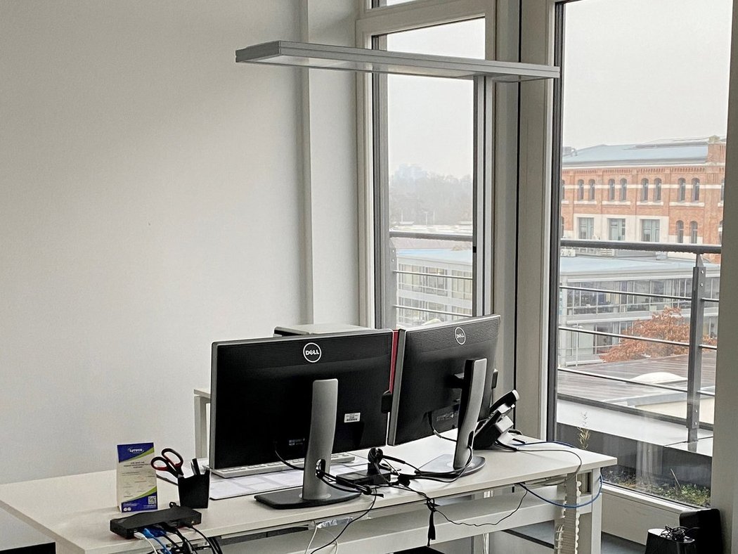 Arbeitsplatz Büro mit zwei Dell-Monitoren auf weißem Schreibtisch, Fensterblick auf Gebäude im Hintergrund