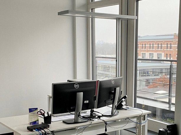 Arbeitsplatz Büro mit zwei Dell-Monitoren auf weißem Schreibtisch, Fensterblick auf Gebäude im Hintergrund